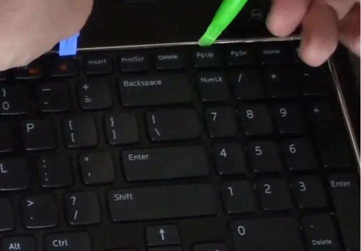 Outil plastique inséré sous le bord supérieur du clavier pour déclipser les languettes